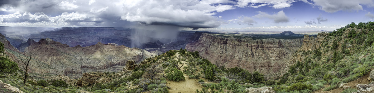 A panorama of the Grand Canyon.  A rain cloud above the Colorado River pours down rain into the canyon.