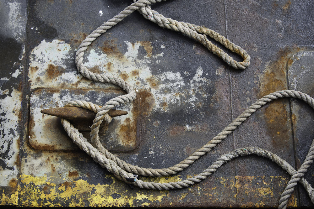 A heavy rope is strewn and snaking over the surface of a dock.  Paint peeling and other signs of wear and tear are evident on the deck.